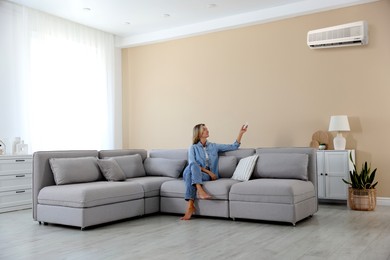 Image of Woman using remote to control air conditioner on sofa at home