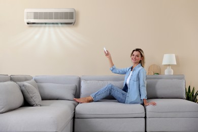 Image of Woman using remote to control air conditioner on sofa at home