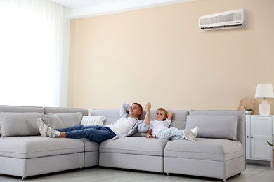 Image of Cute little boy and his father using remote to control air conditioner on sofa at home