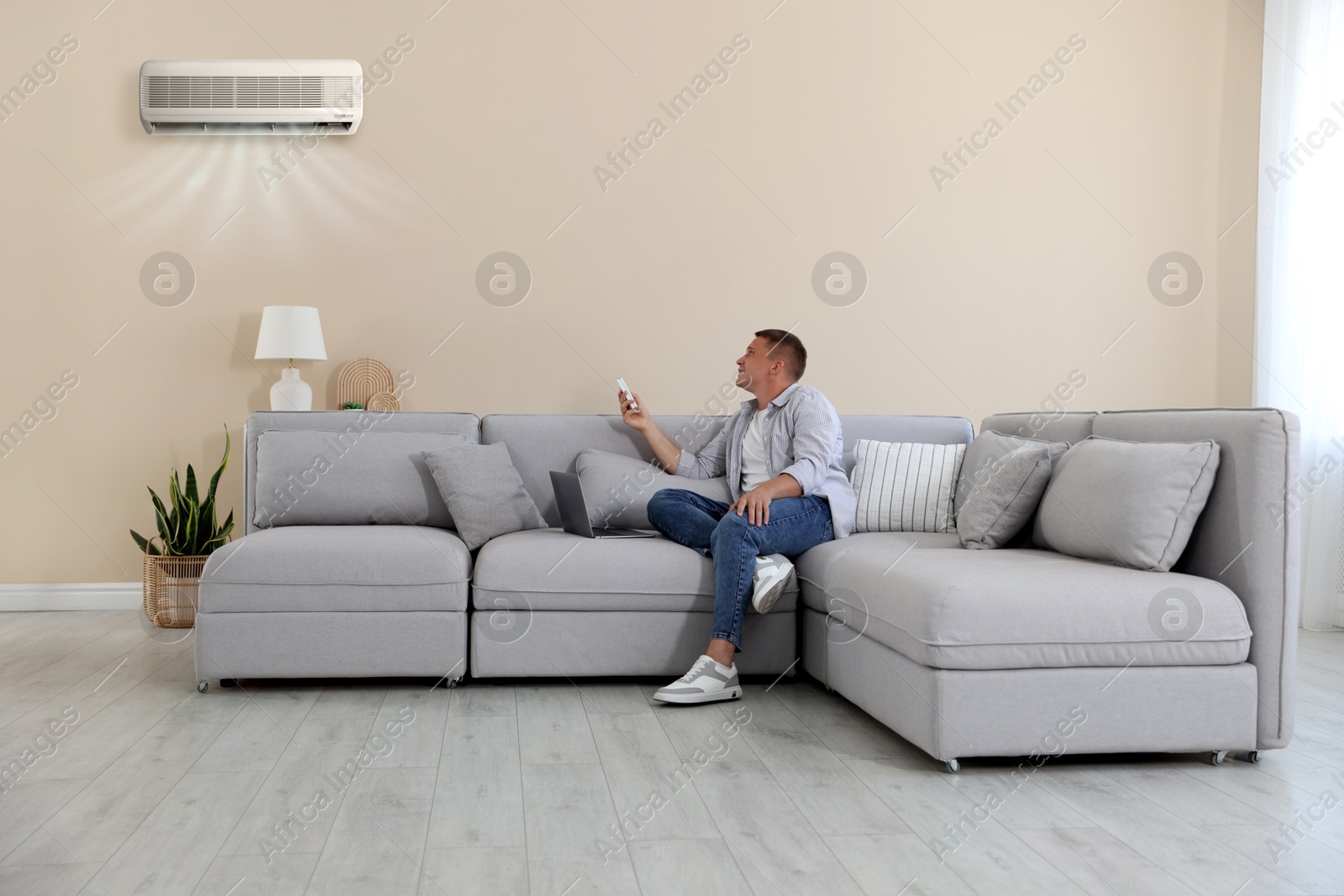 Image of Man using remote to control air conditioner on sofa at home