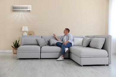 Image of Man using remote to control air conditioner on sofa at home