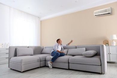 Image of Man using remote to control air conditioner on sofa at home