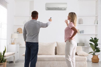 Image of Woman and man using remote to control air conditioner at home