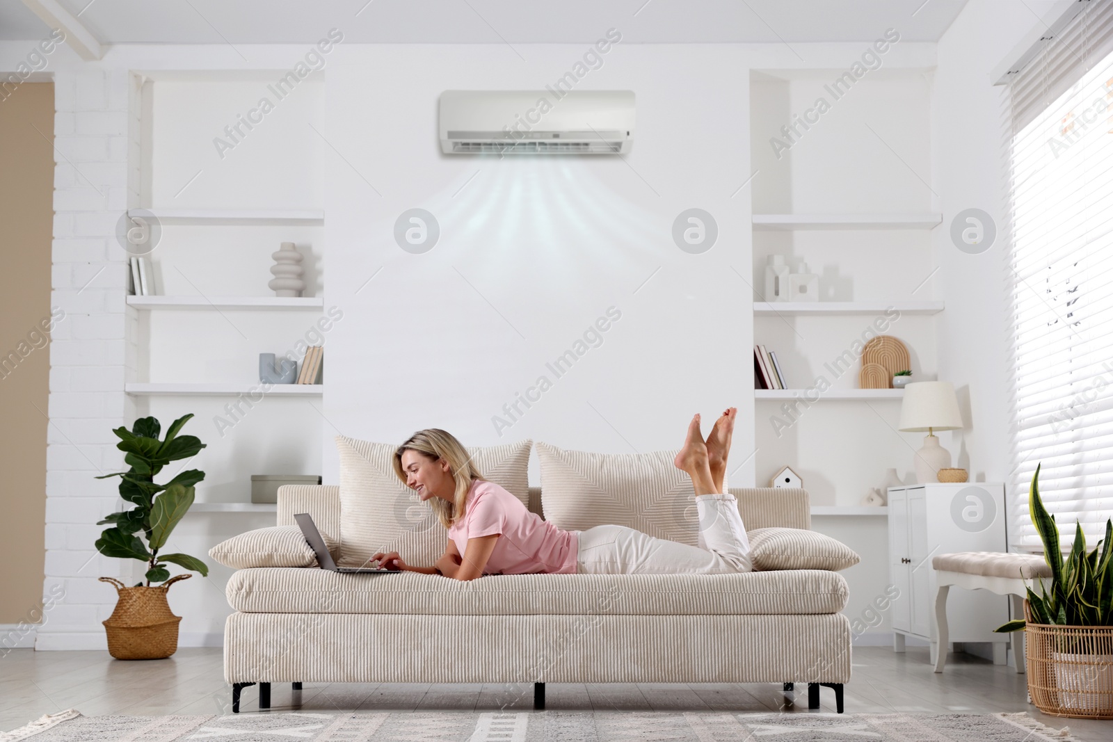 Woman using laptop on sofa in room with air conditioner Image of Woman using laptop on sofa in room with air conditioner