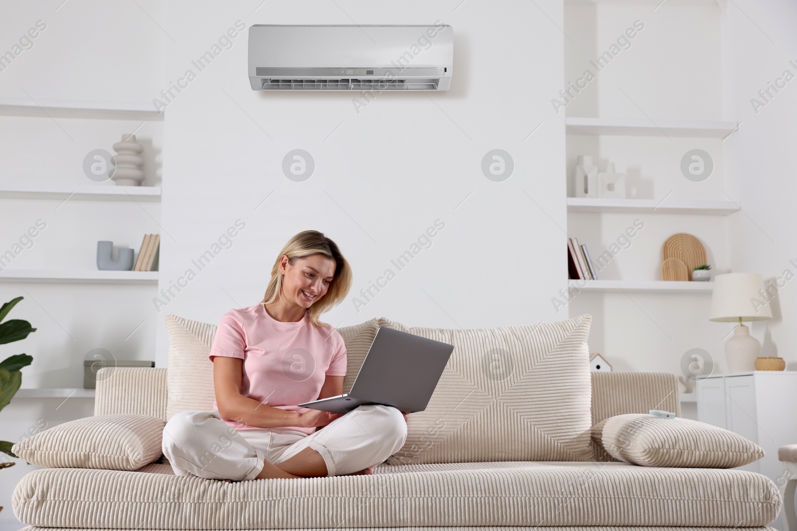 Image of Woman using laptop on sofa in room with air conditioner