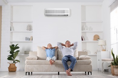 Image of Father and his son enjoying comfortable temperature in room with air conditioner