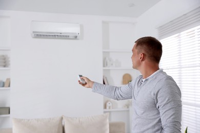 Image of Man using remote to control air conditioner at home