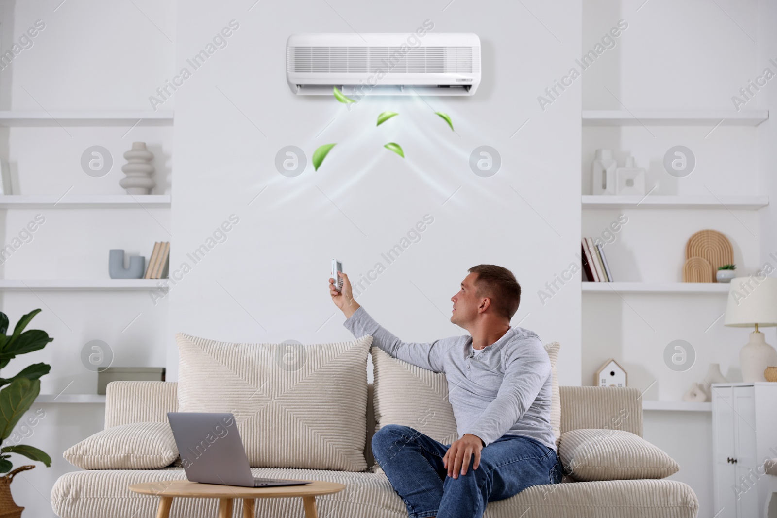 Image of Man using remote to control air conditioner on sofa at home
