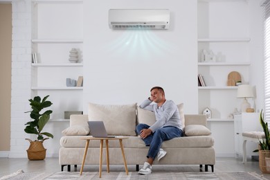Image of Man watching something on laptop in room with air conditioner