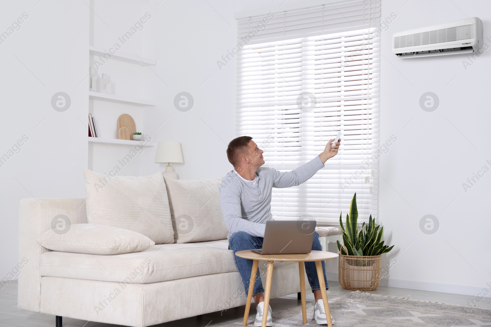 Image of Man using remote to control air conditioner on sofa at home