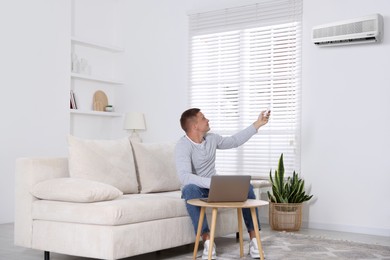 Image of Man using remote to control air conditioner on sofa at home