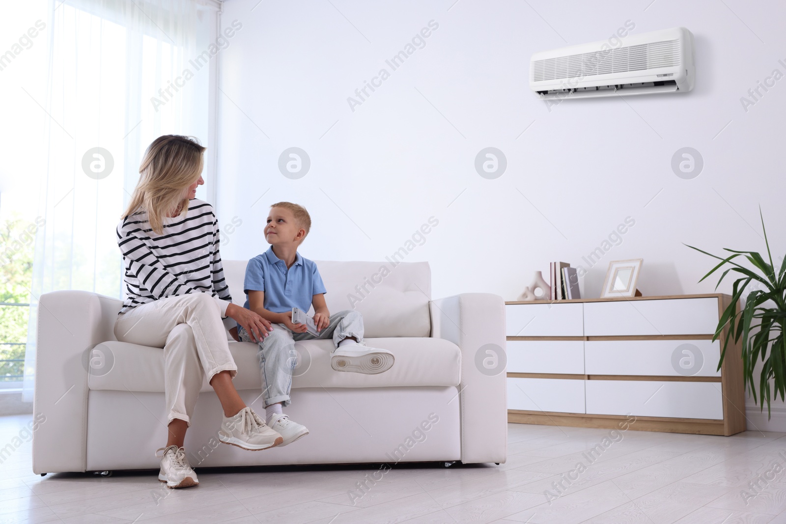 Image of Woman and her son with air conditioner remote control on sofa at home