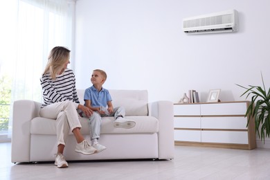 Image of Woman and her son with air conditioner remote control on sofa at home
