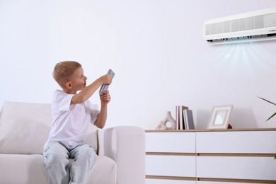 Image of Cute little boy using remote to control air conditioner on sofa at home