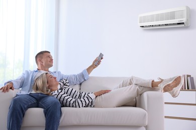 Image of Woman and man using remote to control air conditioner on sofa at home