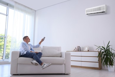 Image of Man using remote to control air conditioner on sofa at home