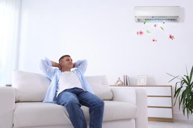 Image of Man enjoying comfortable temperature on sofa in room with air conditioner