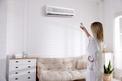Image of Woman using remote to control air conditioner at home