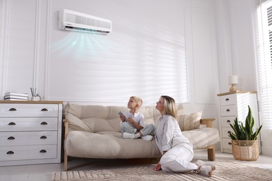 Image of Woman and her son using remote to control air conditioner on sofa at home