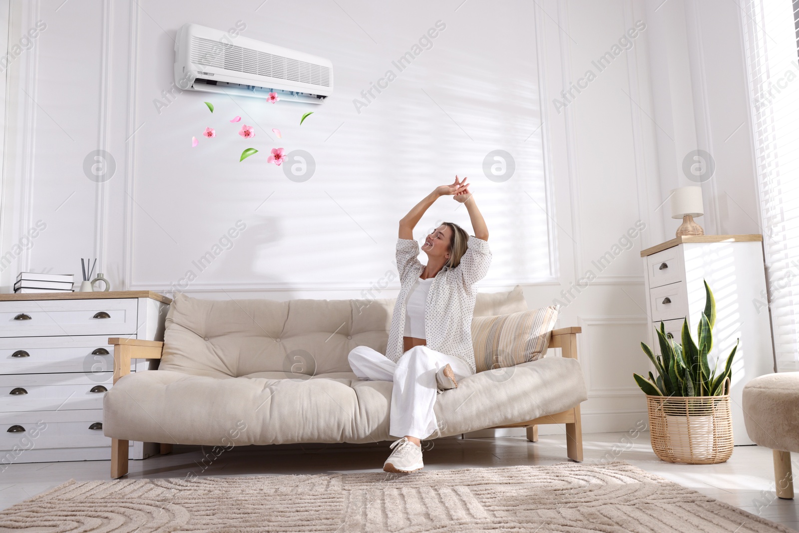 Image of Woman enjoying comfortable temperature on sofa in room with air conditioner