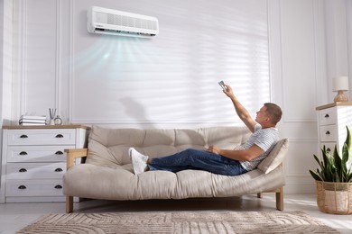 Image of Man using remote to control air conditioner on sofa at home