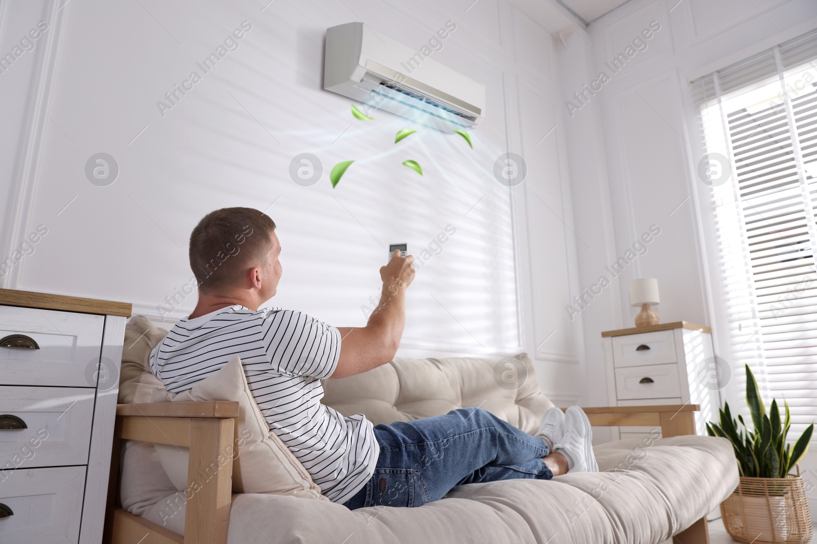 Image of Man using remote to control air conditioner on sofa at home, low angle view