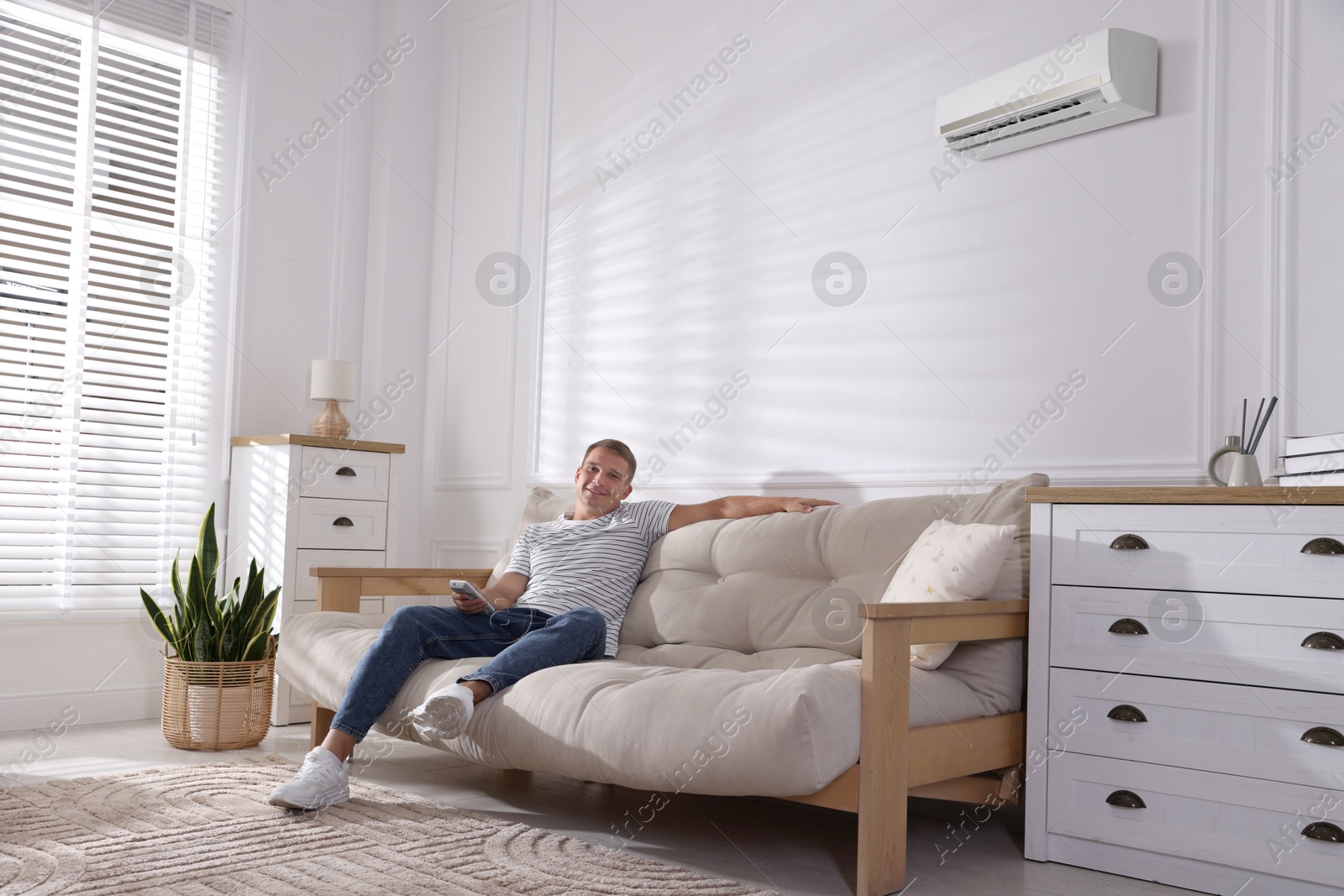 Image of Man with air conditioner remote control on sofa at home