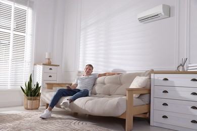 Image of Man with air conditioner remote control on sofa at home