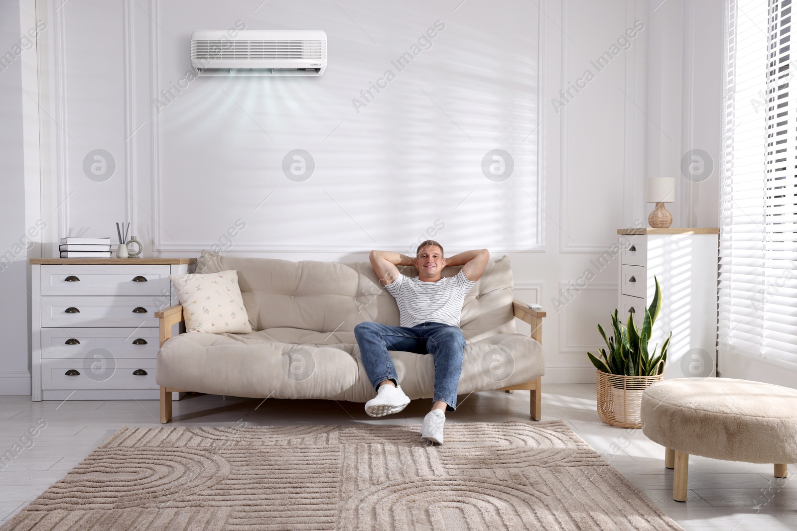 Image of Man enjoying comfortable temperature on sofa in room with air conditioner