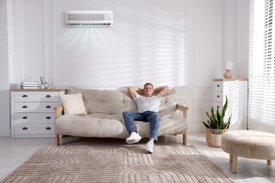Image of Man enjoying comfortable temperature on sofa in room with air conditioner