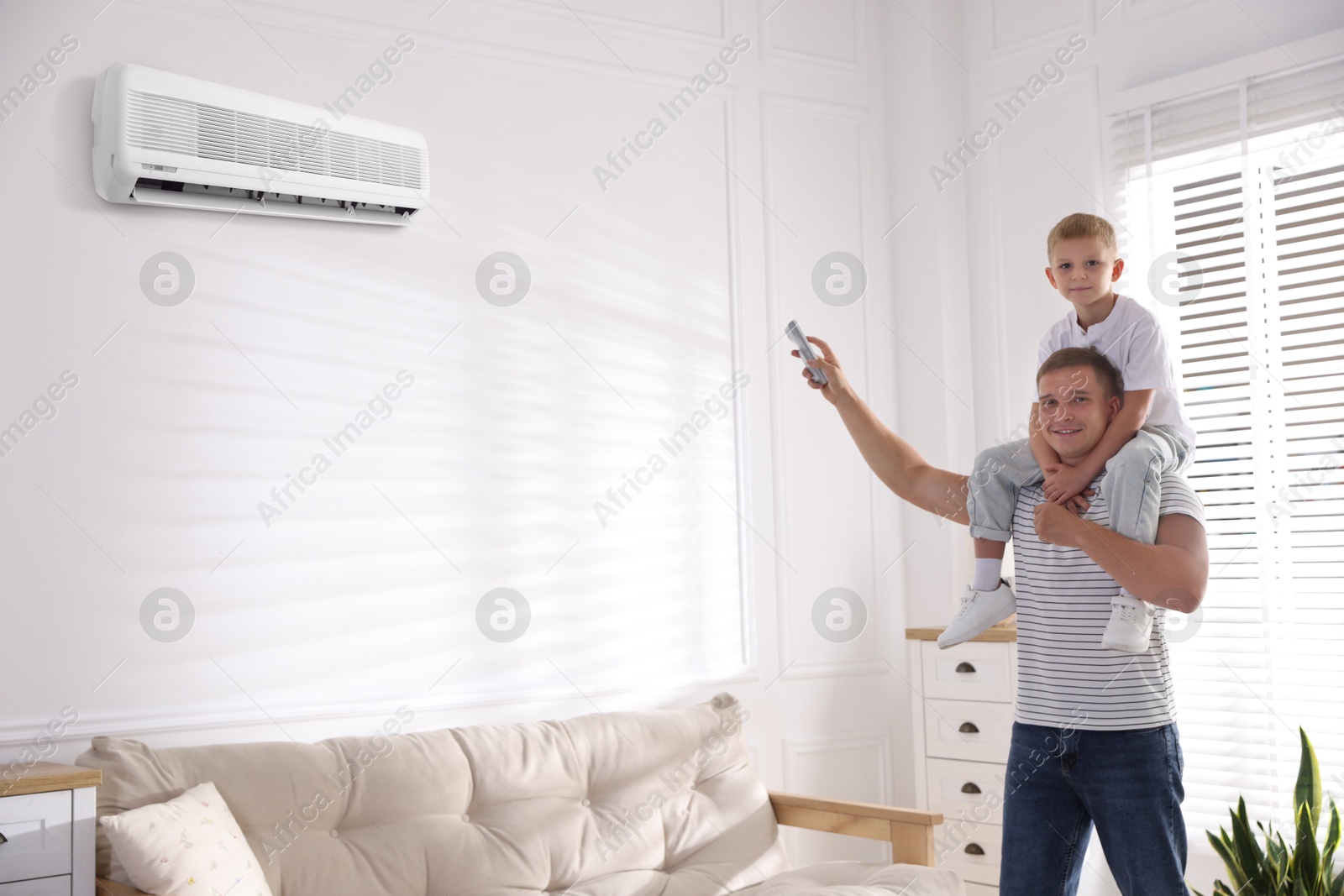 Little boy and his father using remote to control air conditioner at home Image of Little boy and his father using remote to control air conditioner at home