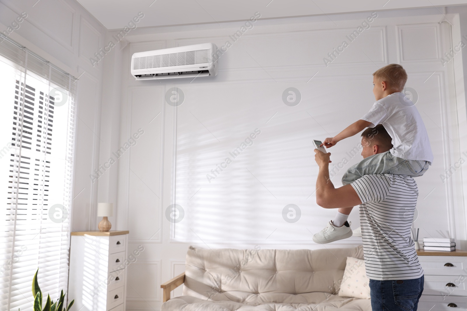 Little boy and his father using remote to control air conditioner at home Image of Little boy and his father using remote to control air conditioner at home