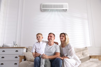 Image of Woman with air conditioner remote control, her husband and son on sofa at home