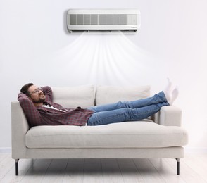 Image of Happy man relaxing on sofa at home. Air conditioner keeping comfortable temperature in room