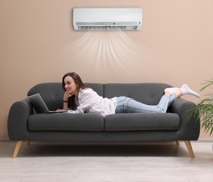 Image of Smiling woman with laptop lying on sofa at home. Air conditioner keeping comfortable temperature in room