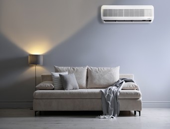 Image of Air conditioner, sofa with pillows, blanket and lamp in room