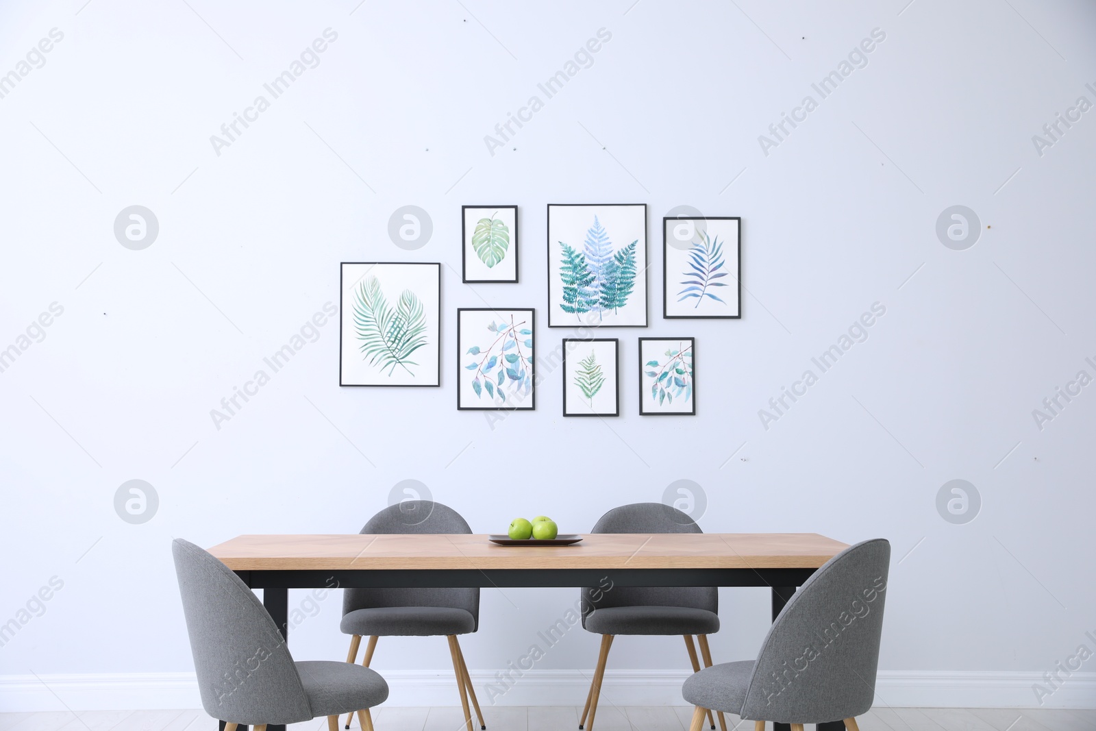 Photo of Stylish room interior with modern table, chairs and paintings of tropical leaves. Idea for design