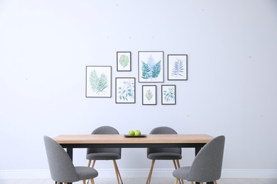 Photo of Stylish room interior with modern table, chairs and paintings of tropical leaves. Idea for design