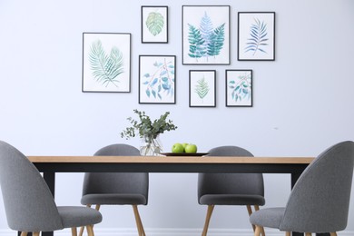 Photo of Stylish room interior with modern table, chairs and paintings of tropical leaves. Idea for design