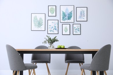 Photo of Stylish room interior with modern table, chairs and paintings of tropical leaves. Idea for design