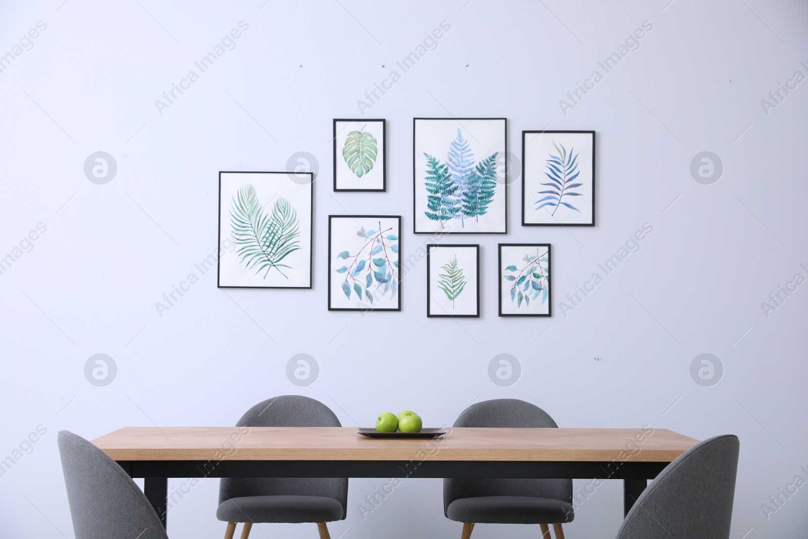 Photo of Stylish room interior with modern table, chairs and paintings of tropical leaves. Idea for design