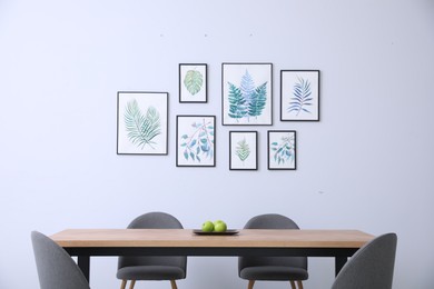 Photo of Stylish room interior with modern table, chairs and paintings of tropical leaves. Idea for design