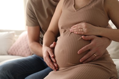 Photo of Man touching his pregnant wife's belly at home, closeup