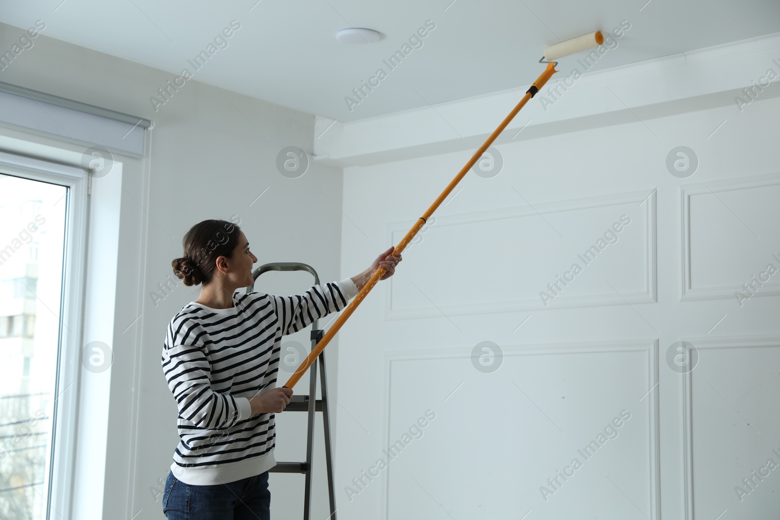 Young woman painting ceiling with white dye indoors, space for text Photo of Young woman painting ceiling with white dye indoors, space for text