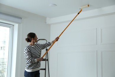 Photo of Young woman painting ceiling with white dye indoors, space for text