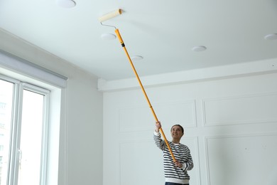 Photo of Young woman painting ceiling with white dye indoors, space for text