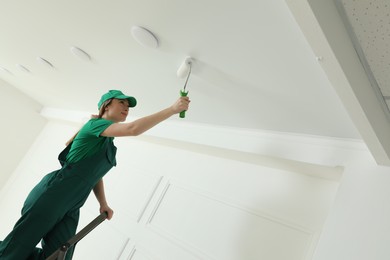 Photo of Worker painting ceiling with white dye indoors, space for text