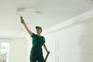 Photo of Worker painting ceiling with white dye indoors, space for text
