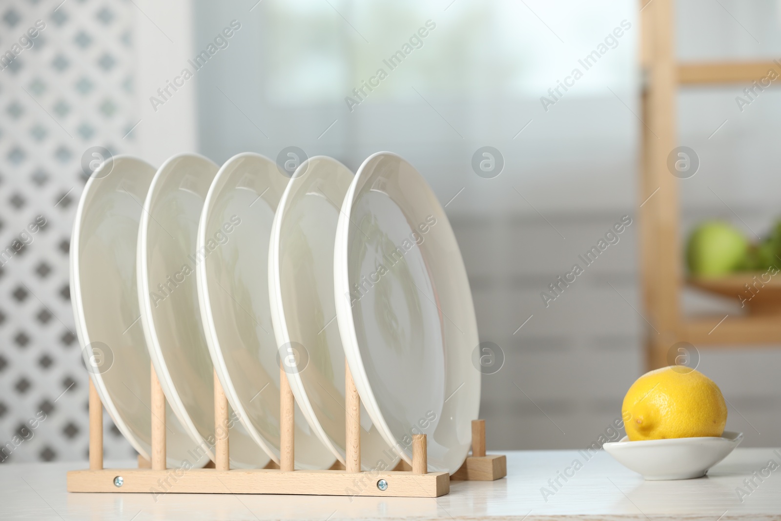 Photo of Clean plates in dish drying rack and lemon on white table indoors