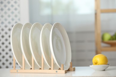 Photo of Clean plates in dish drying rack and lemon on white table indoors
